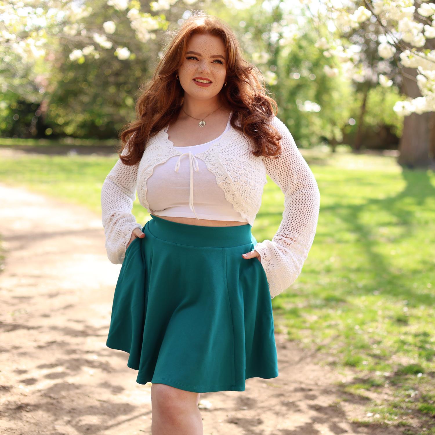 Woman wearing a white top and teal skirt standing outdoors with trees in the background